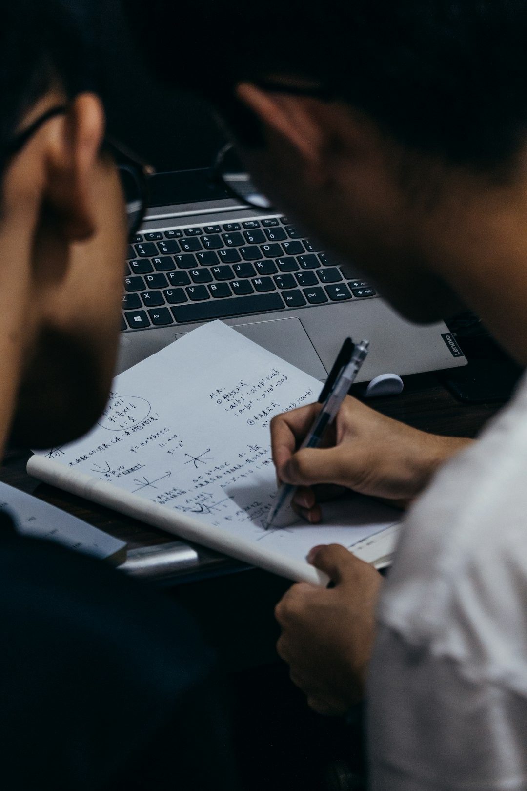 Two people working and writing math equations and Chinese characters at a desk.