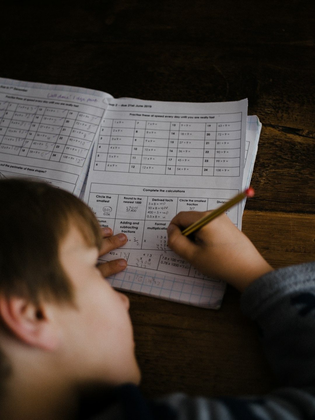 Child's hands holding yellow pencil on math worksheet.